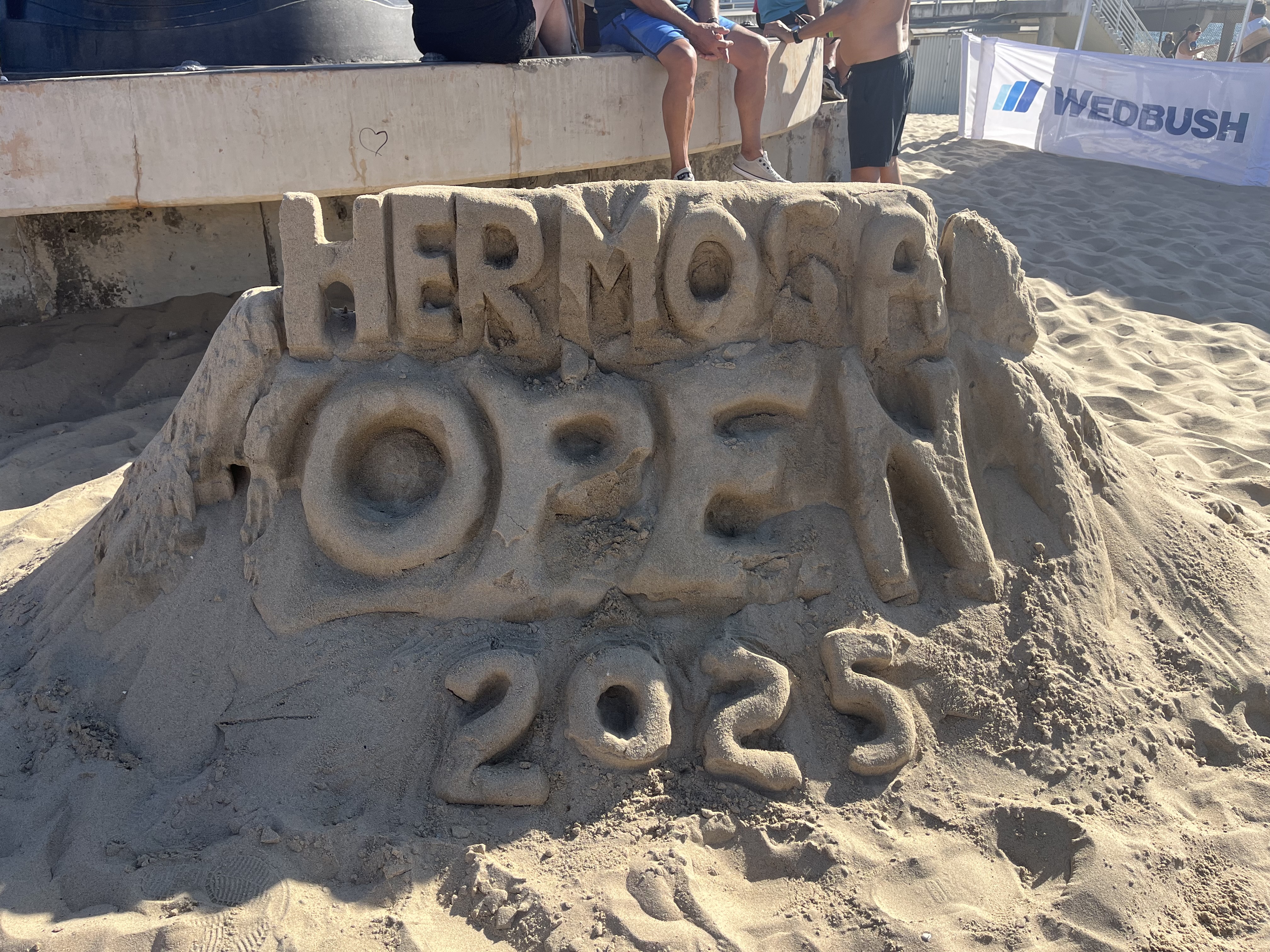 A sand sculpture reading &ldquo;Hermosa Open 2025&rdquo; on the beach.